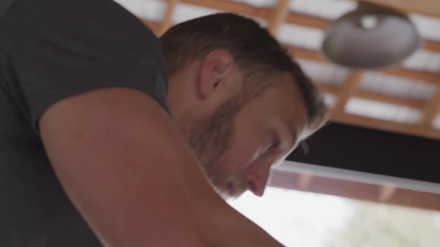 A man on a spinning machine cycles at a high intensity indoors in daylight
