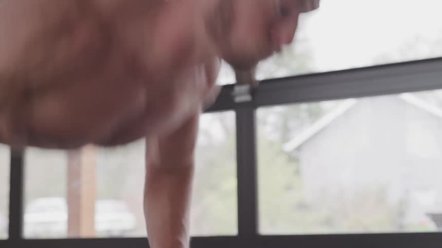 Shirtless man does push ups near window