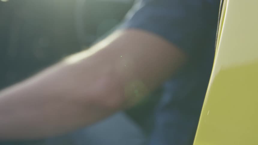 A man shuts the door of a yellow vehicle