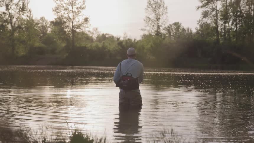 A man stands in a lake and reels in his fishing rod