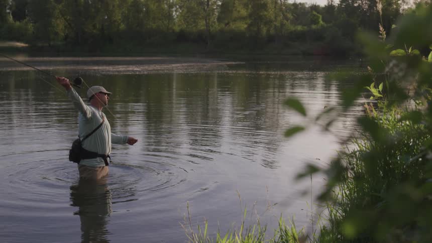 A fisherman standing in a body of water while casting a fishing line