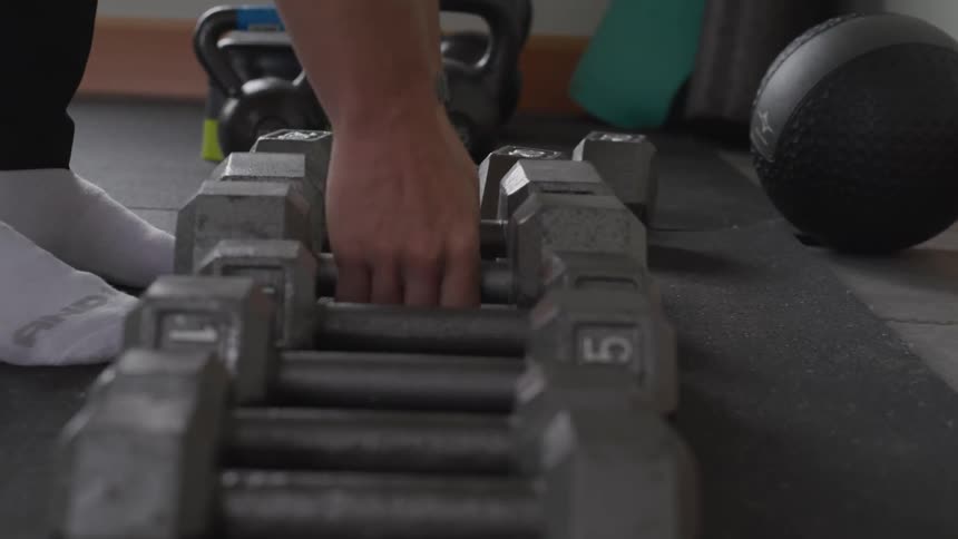 A person puts down two dumbbells in a row of dumbbells on a gym floor