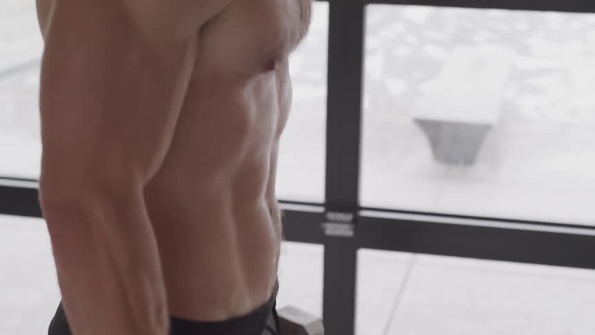 A shirtless white man lifts dumbbells indoors