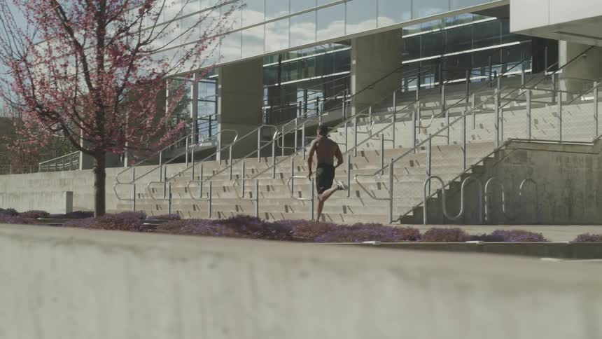 A shirtless man running on the sidewalk in front of a building on a sunny day