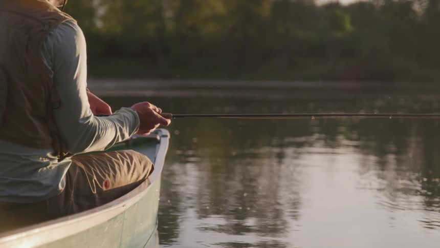 A woman sits in a canoe holding a fishing pole on a tranquil lake