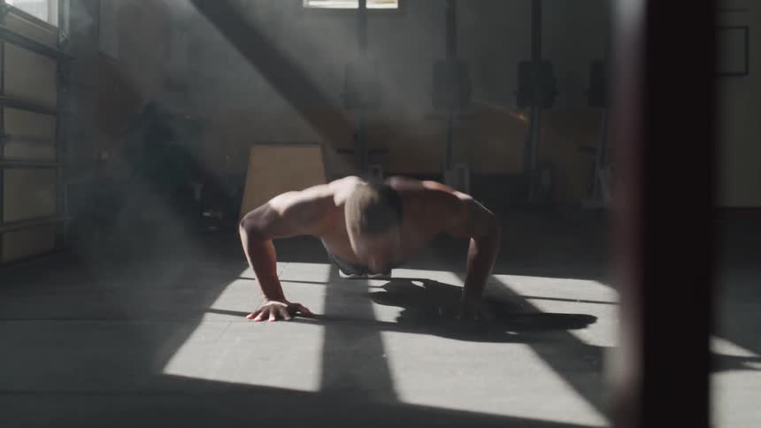 A person does pushups in a dark gym