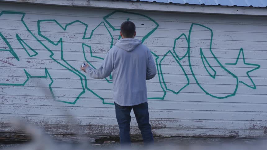 Man shaking a can in front of a wall with graffiti