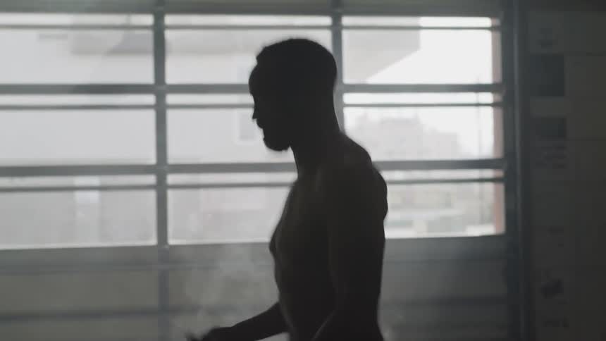 A shirtless and muscular black male begins to jump rope for exercise inside of a garage