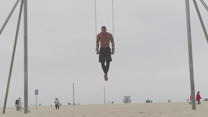 A man uses gymnastic rings for strength training on a beach