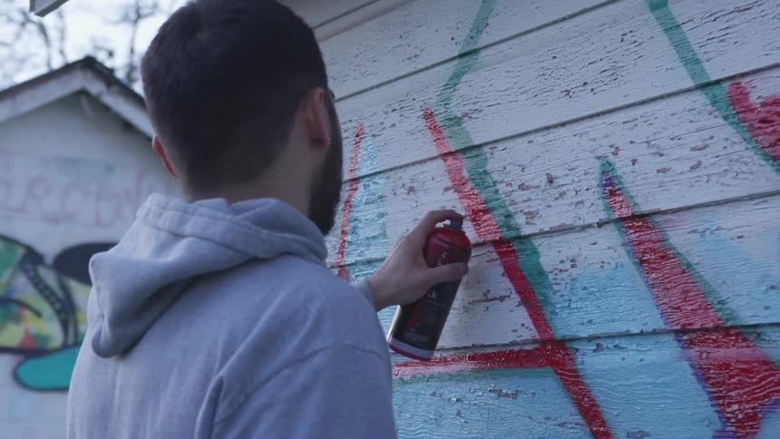 Man sprays graffiti on white painted wood siding