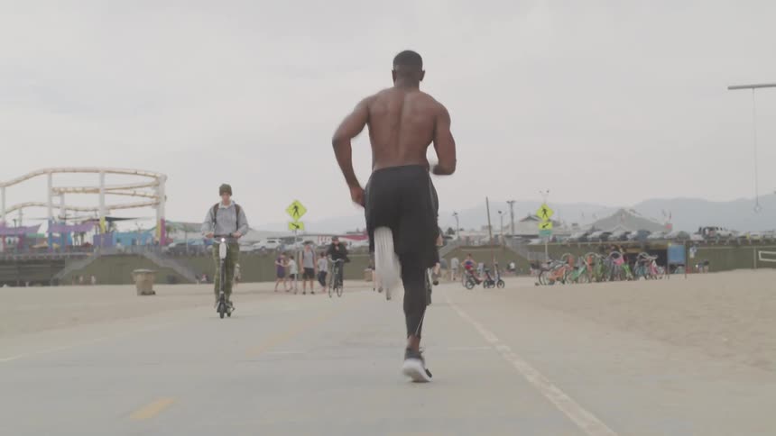 Shirtless muscular black man runs on the road through the beach on a cloudy day