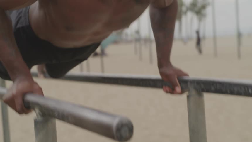 A muscular man doing push ups on parallel bars at the beach