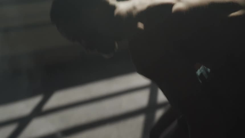 A shirtless man jumps up and down then bends to lift heavy dumbbells for bicep curls