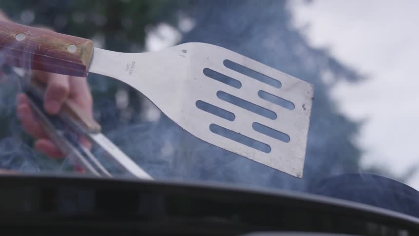 Hamburger patty being flipped with tongs on an outdoor grill