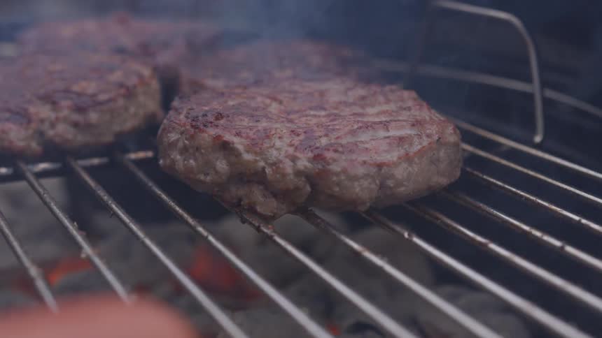 Beef patties being barbecued on an open girl using charcoal during the day