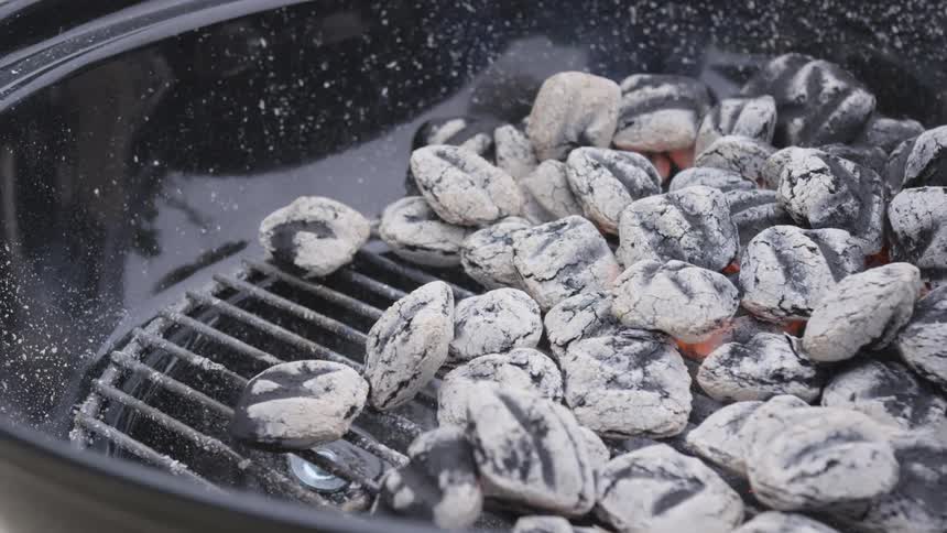 Lit charcoals in a barbecue grill with smoke coming off of them