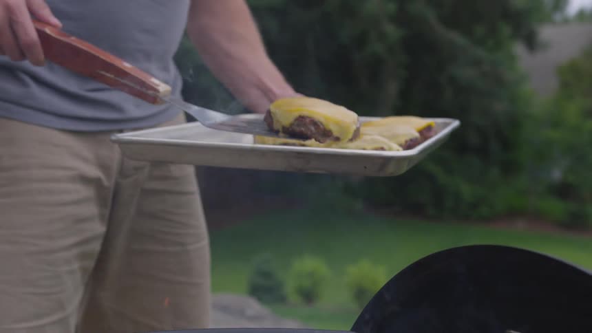 A man picks up a cheeseburger from the grill and places it on a tray with other cheeseburgers