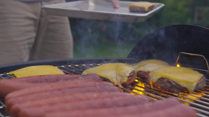 Cheese hamburgers and hot dogs being grilled outdoors