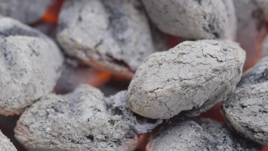 Fire glows from within pile of charcoal briquettes that are turning to ash