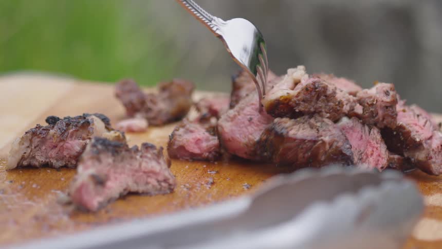 A strip of sliced beef being lifted from a cutting board with a fork