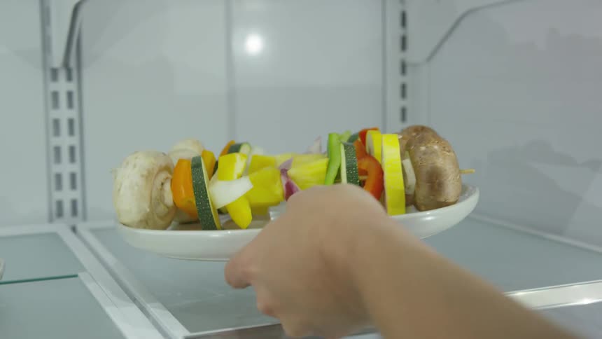 Vegetable kabobs on a white plate being picked up from refrigerator