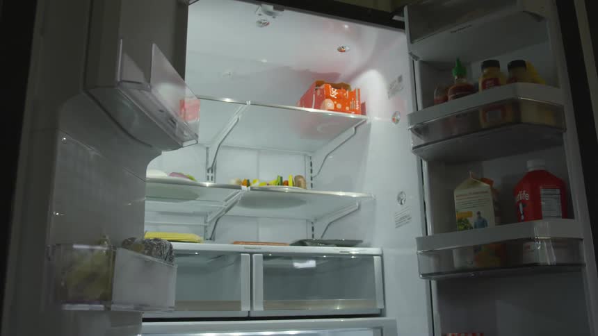 A refrigerator with double doors is left open in a darkened kitchen and several items are present on the refrigerator shelves