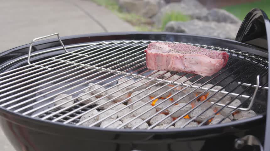 A man puts a seasoned steak on a hot charcoal grill
