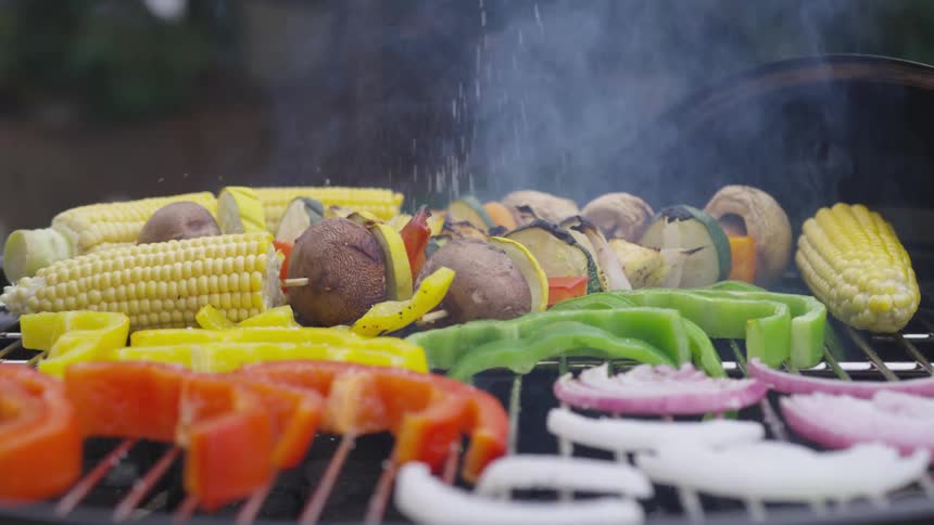 Seasoning is being sprinkled on the vegetables on the barbecue