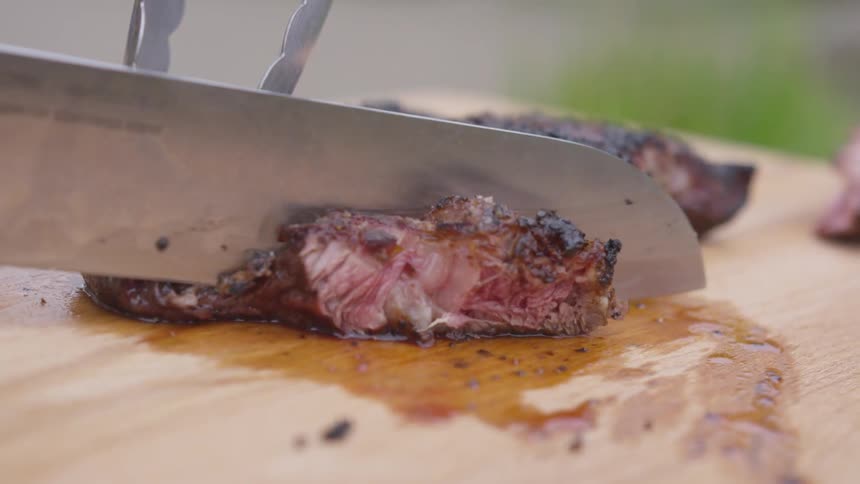 Greasy meat being cut on a wooden cutting board