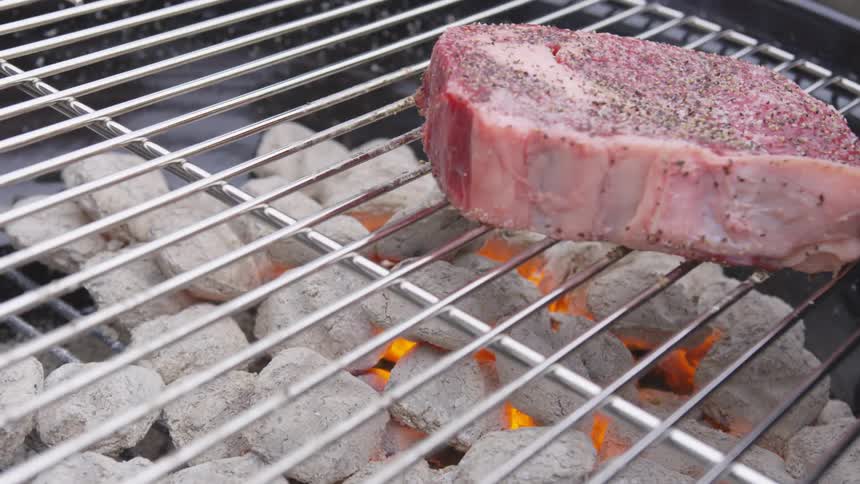 Meat being dropped on a barbecue grill with lit charcoals