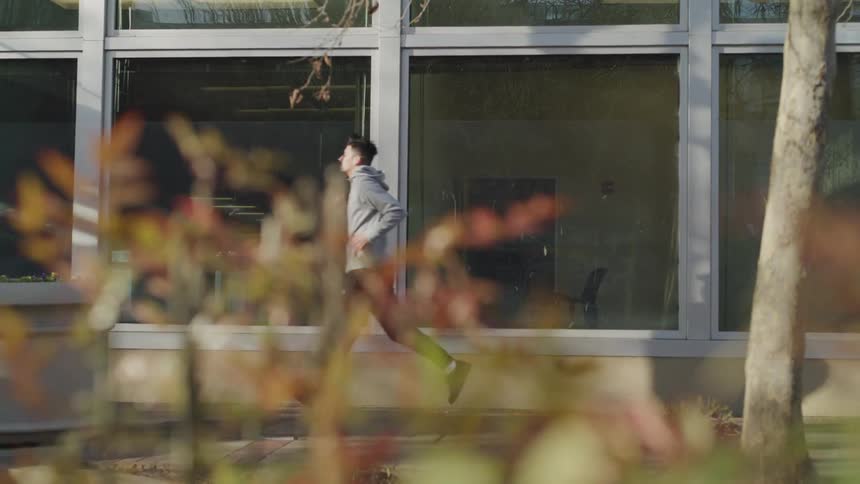 A man with a gray hoodie jogging in front of a building