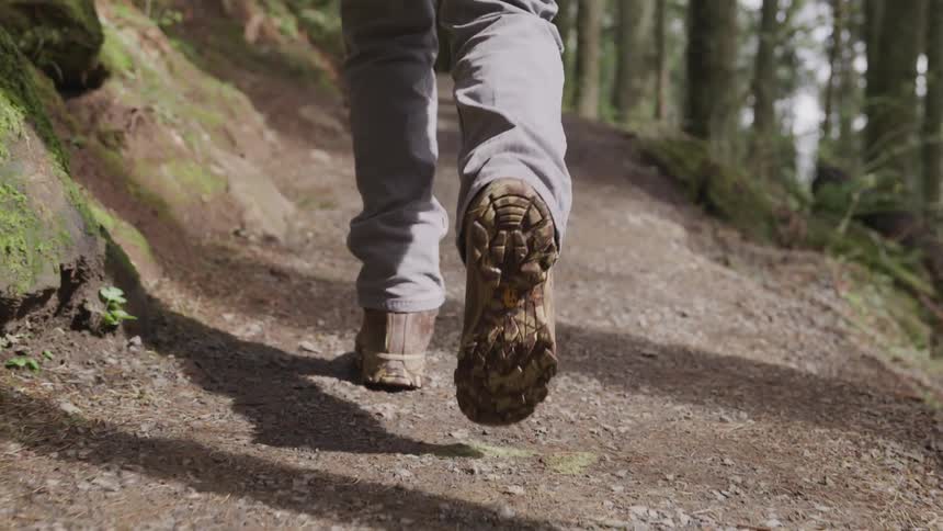 The dirty treads of hiking boots as a person walks on a narrow forest trail on a sunny day