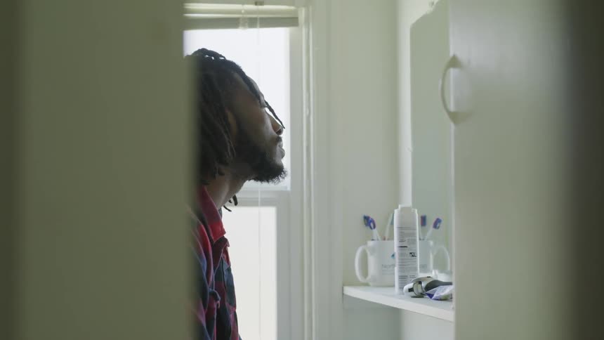 Man stands in the bathroom and lifts his head to look in the mirror
