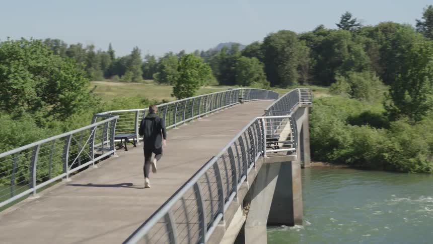 Man runs along bridge over river during sunny day