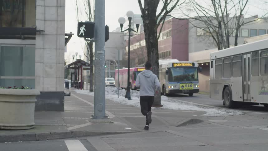 A man runs on the sidewalk next to a street filled with buses used for public transportation