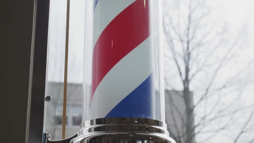 A red white and blue barber pole is spinning slowly in a window with a bare tree in the background