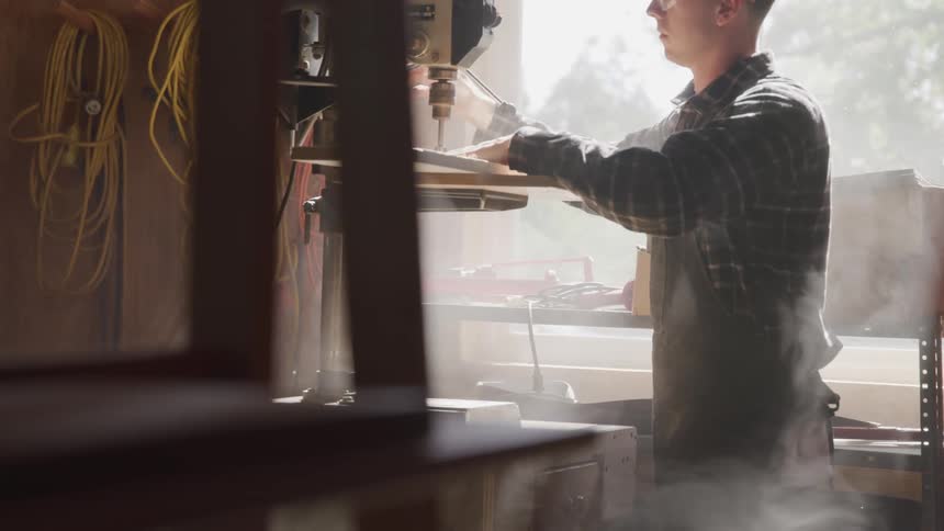 A man uses a machine to drill wood in a shop