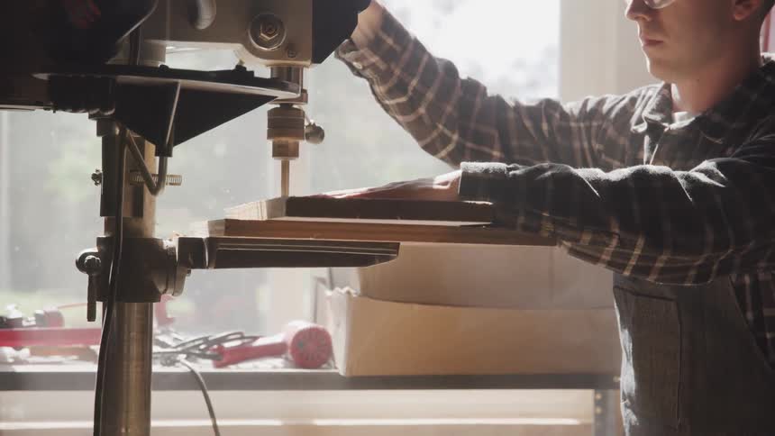 A man uses a machine to drill through wood