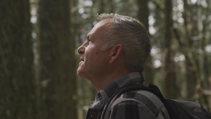 Man standing in middle of forest looking up talking to himself