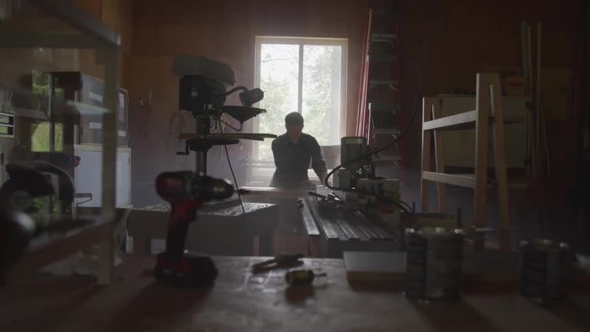 A man working in a workshop lit by a window behind him