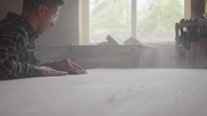 Man wearing safety glasses rubs a table top with a sponge
