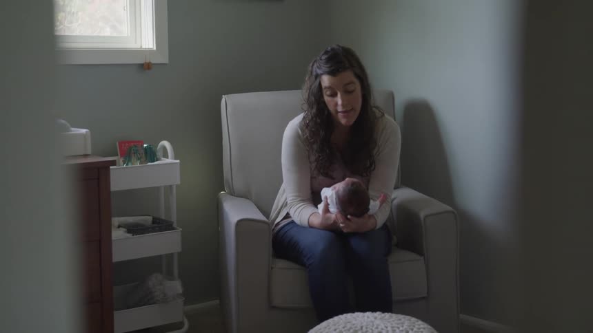 A young woman holds a baby and looks down and talks to it