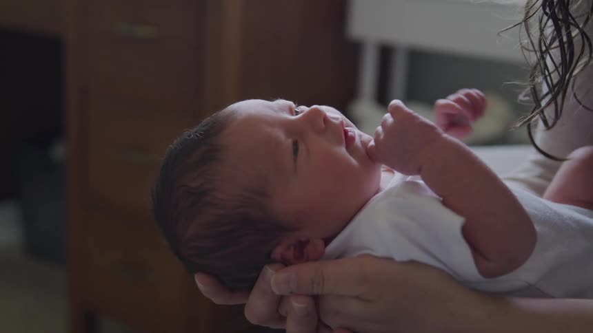 Wiggling baby in white onesie lies in his mothers arms