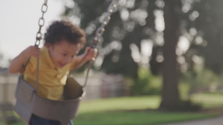 Mother pushing her little boy on swings at the park