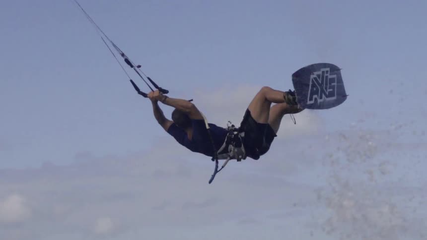 A man navigates a sailboard through water, performing a wind-surfing move across waves.