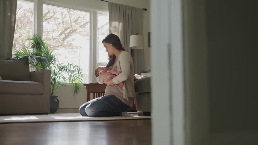 A woman kneels on the floor and rocks a baby in her arms