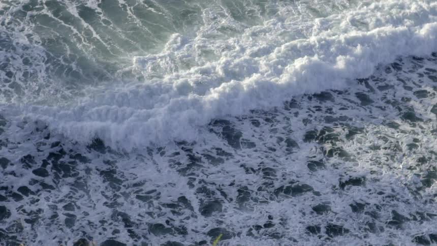 Ocean Waves Wash Ashore Along Sandy Beach Under Bright Natural Daylight and Gentle Breeze.