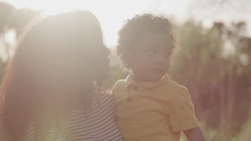 A mother holds and kisses her young son outside on a sunny day