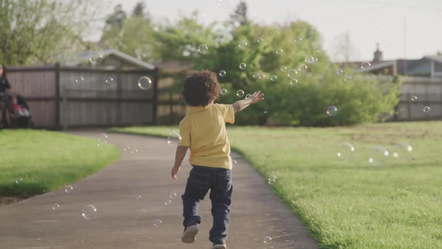 A young boys runs along a sidewalk chasing bubbles