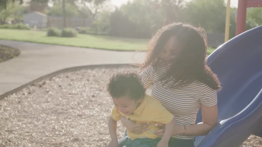 A woman and young boy slide down a slide in a park